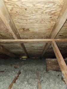 This wooden attic space, resembling a rustic gallery, features charming exposed beams and insulation on the floor.