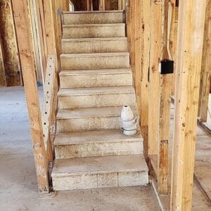 An unfinished wooden staircase at a construction site serves as an unexpected gallery piece, with an upside-down plastic bottle perched artfully on the second step.